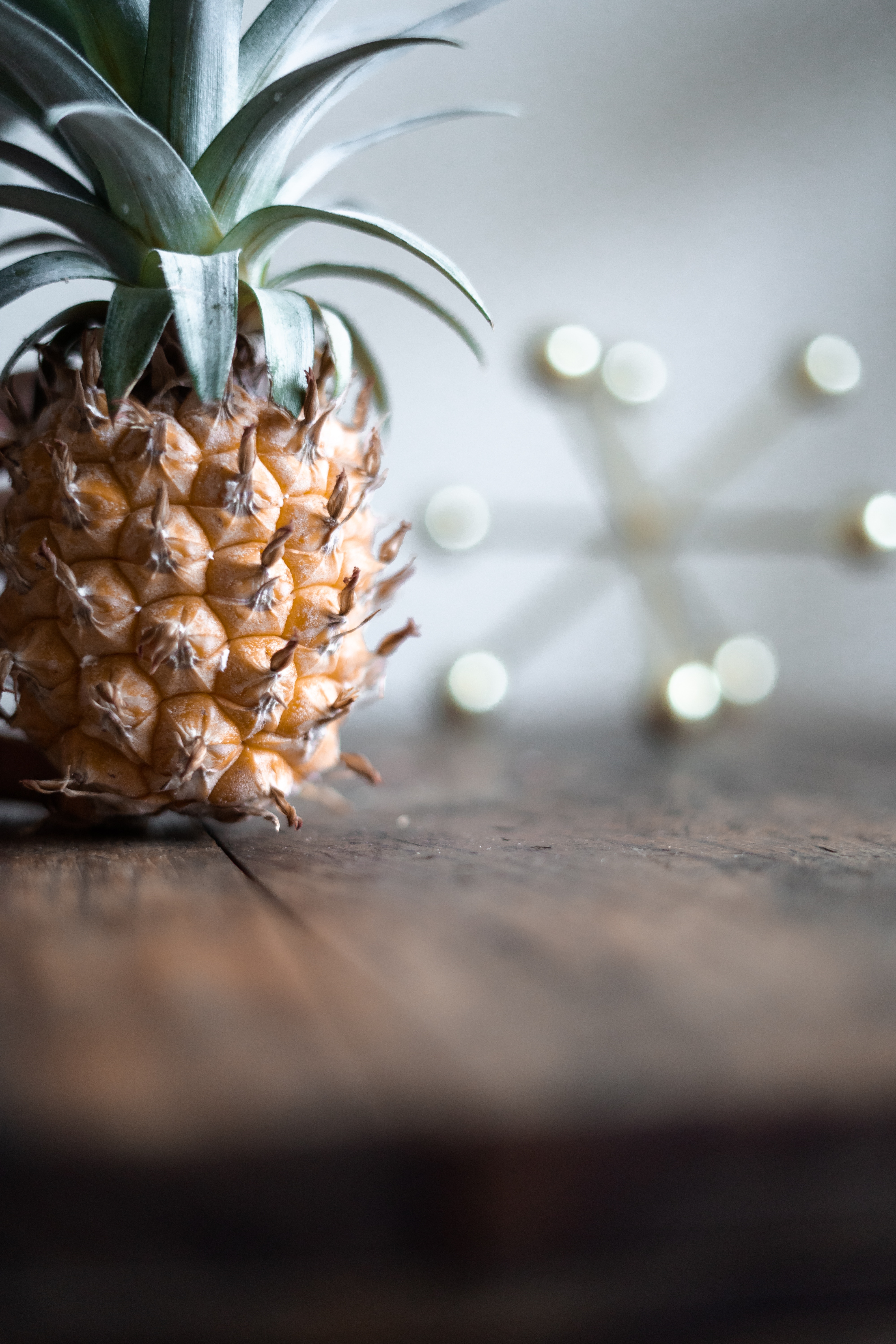Pineapple on wooden table to the left with out of focus decorative piece to the right, all with a white background.